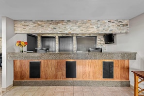 A reception area with a stone mosaic wall, a wooden panel design, and a flat-screen TV mounted on the wall. - Days Inn & Suites by Wyndham Des Moines Airport (Des Moines)