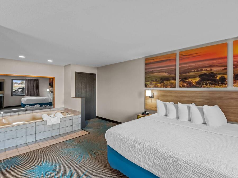A hotel room with a large bed, a bathtub, a mirror, and a sunset painting on the wall.