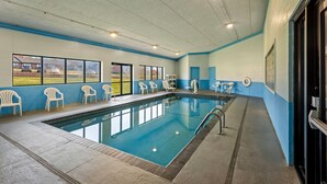 Una piscina interior con ventanas amplias, sillas blancas y una decoración en blanco y azul.