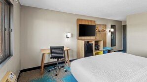 Habitación de hotel con cama, escritorio, silla, televisor y armario.