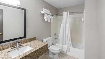 A bathroom with a granite countertop sink, a toilet, a bathtub, and a shower curtain.