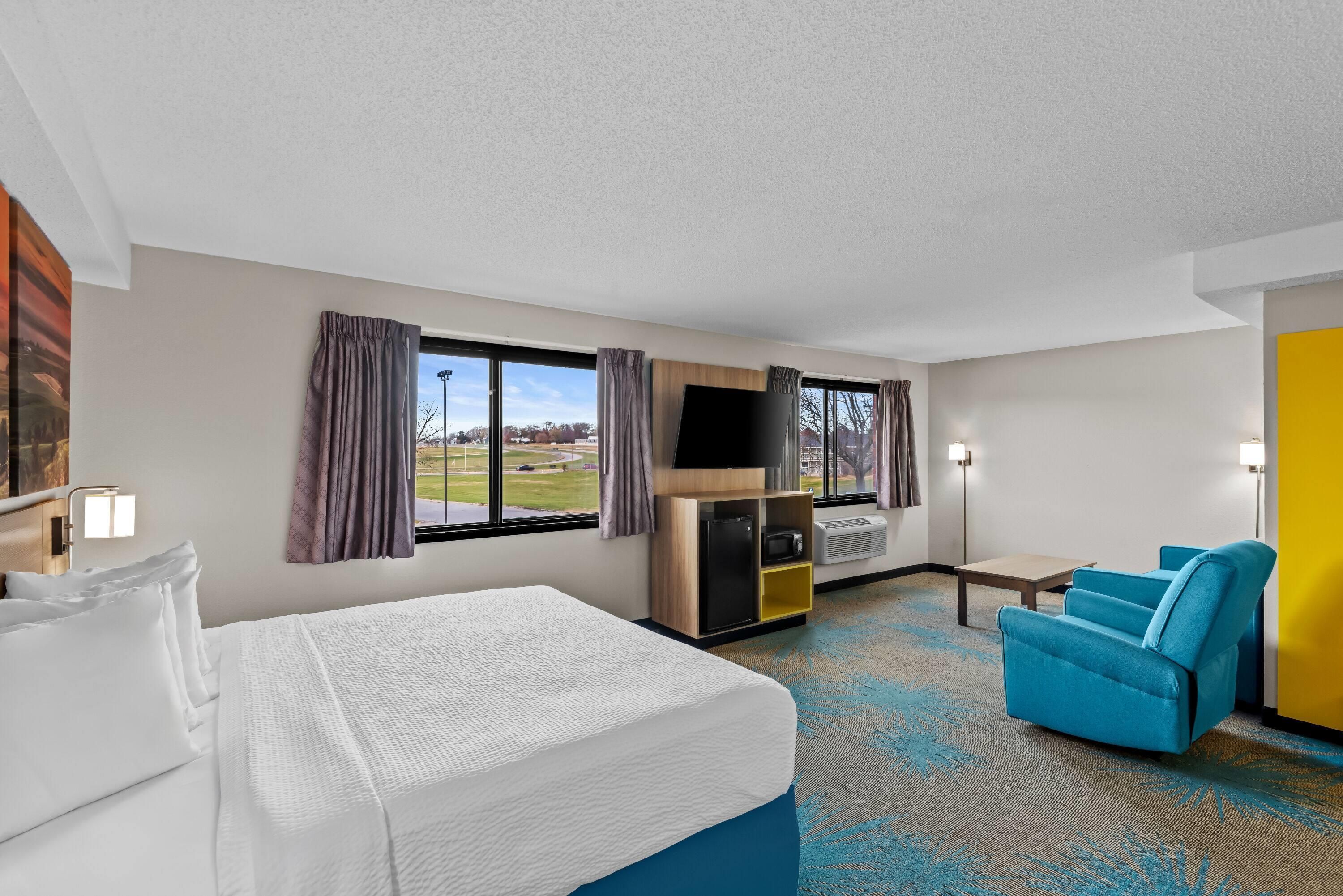 A hotel room with a bed, a desk, a chair, a TV, and a view of the outdoors.