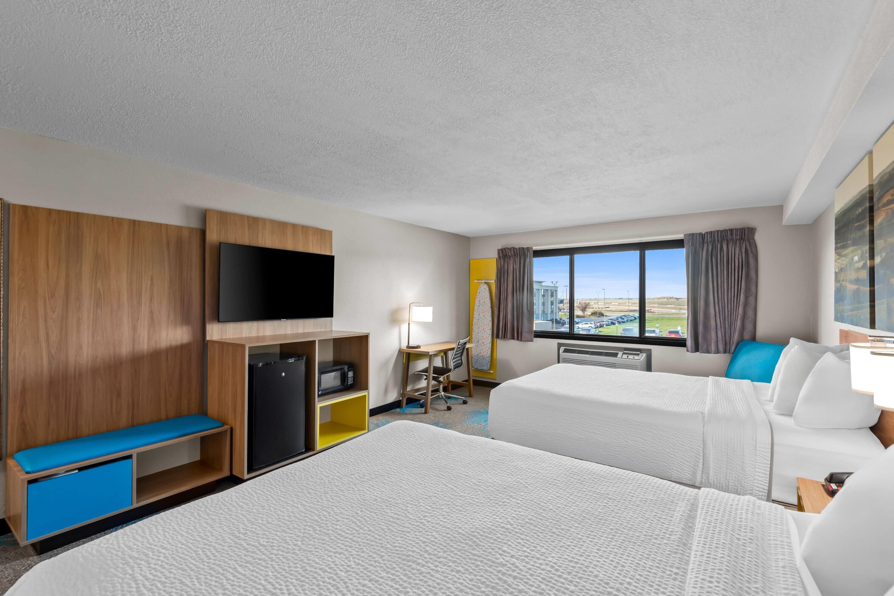 A hotel room with two beds, a desk, a TV, and a view of the city.