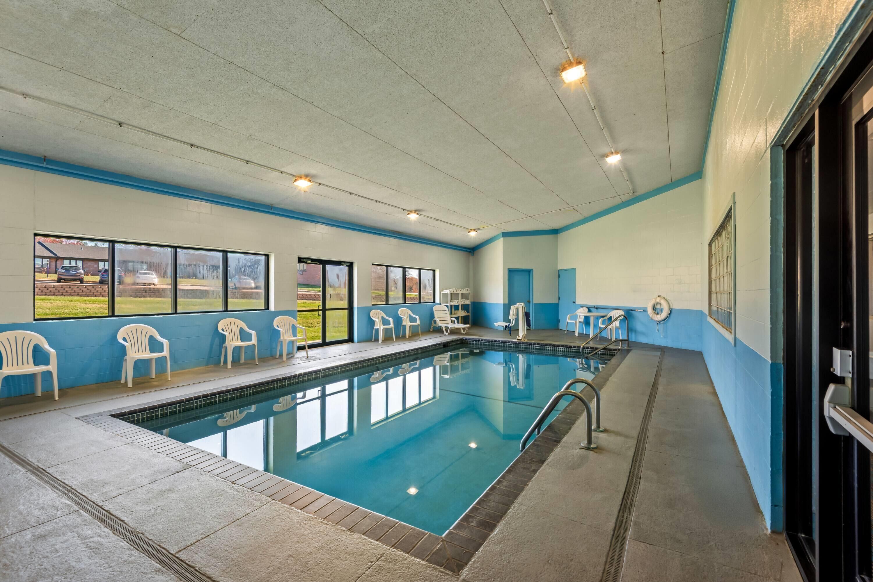 Una piscina interior con ventanas amplias, sillas blancas y una decoración en blanco y azul.