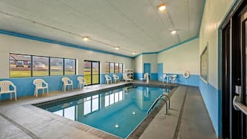 Una piscina interior con ventanas amplias, sillas blancas y una decoración en blanco y azul.