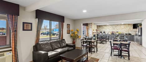 A hotel lobby with a leather sofa, dining area, kitchen, and large windows with curtains.