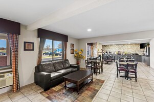 Un hall de hotel con un sofá de cuero, comedor, cocina y ventanas amplias con cortinas.