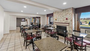 A restaurant with multiple tables and chairs, a fireplace, and a view of the outdoors. - Days Inn & Suites by Wyndham Des Moines Airport (Des Moines)