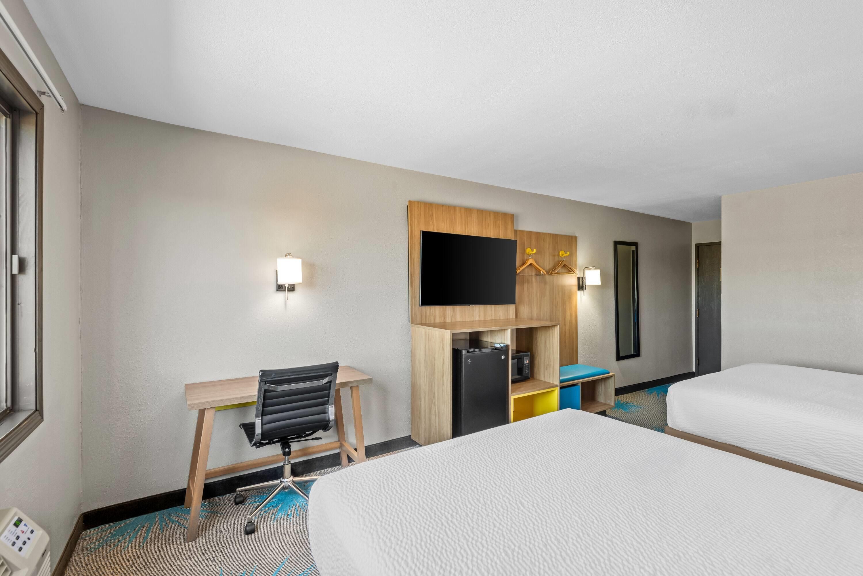 Une chambre d’hôtel comprenant un lit, un bureau avec une chaise, un téléviseur fixé au mur et un petit réfrigérateur.