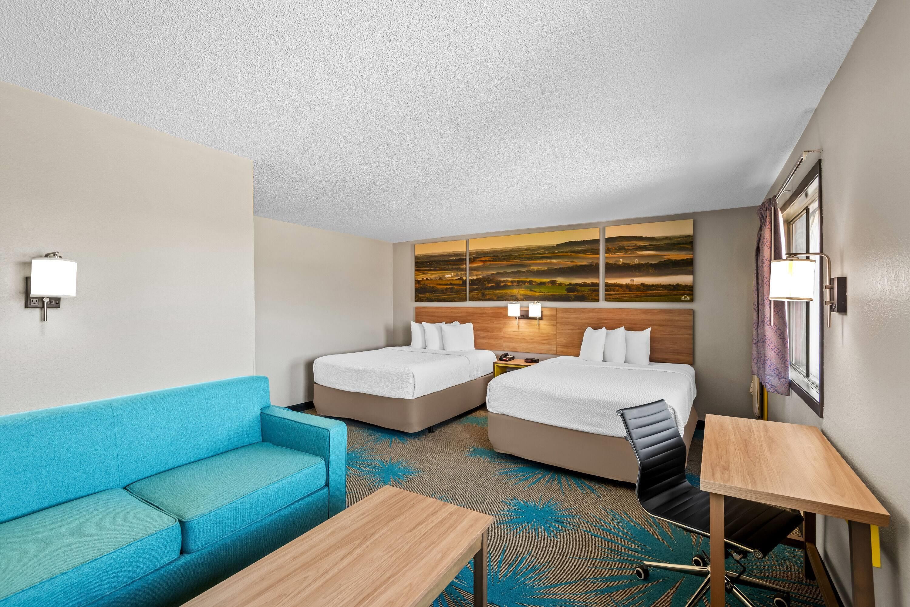Een hotelkamer met twee bedden, een blauwe bank, een houten tafel en een groot landschap op de muur.