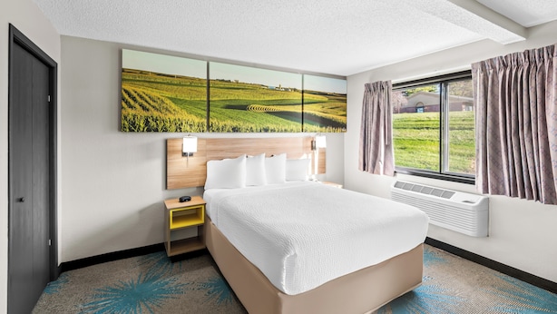Habitación de hotel con una cama grande, una mesita de noche, televisor montado en la pared y una ventana con cortinas.