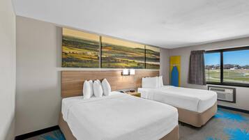 A hotel room with two beds, a large landscape painting, a view of the outdoors, and a window with curtains.