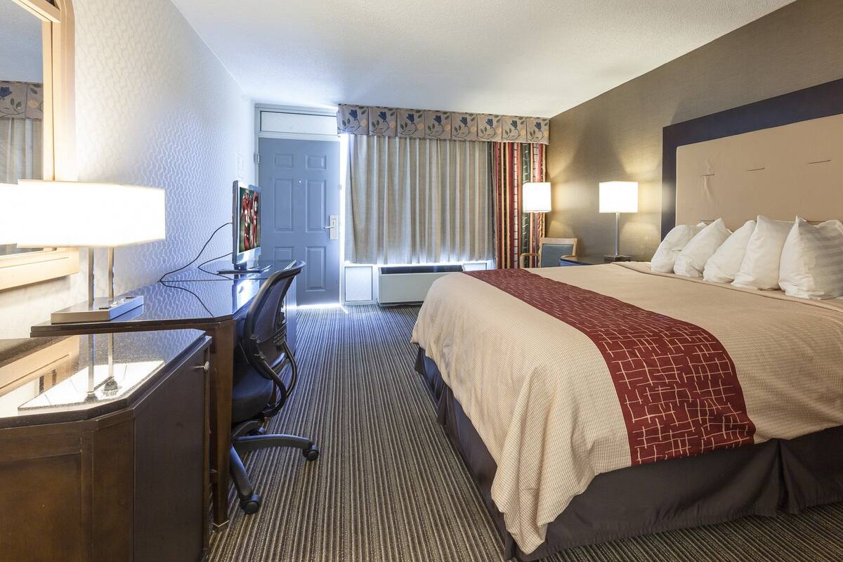 A hotel room with a large bed, a desk with a chair, a TV, and a window with curtains.