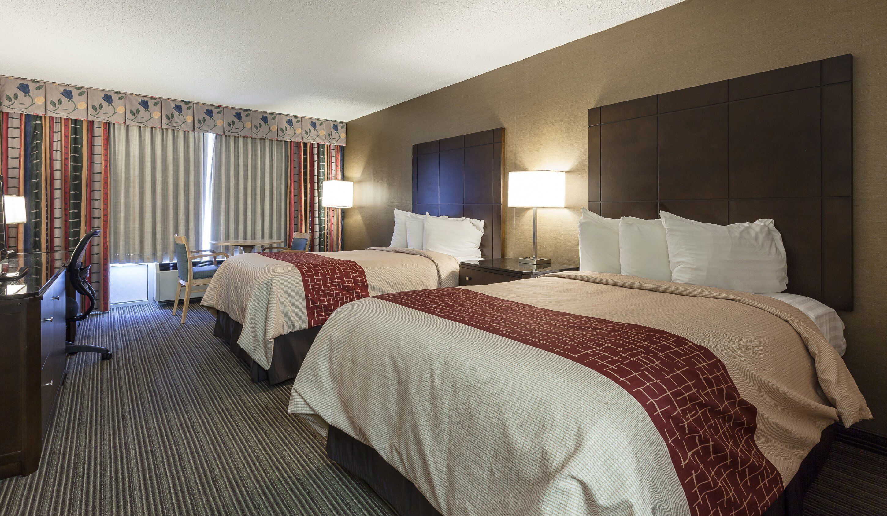 A hotel room with two beds, a desk, and a chair.