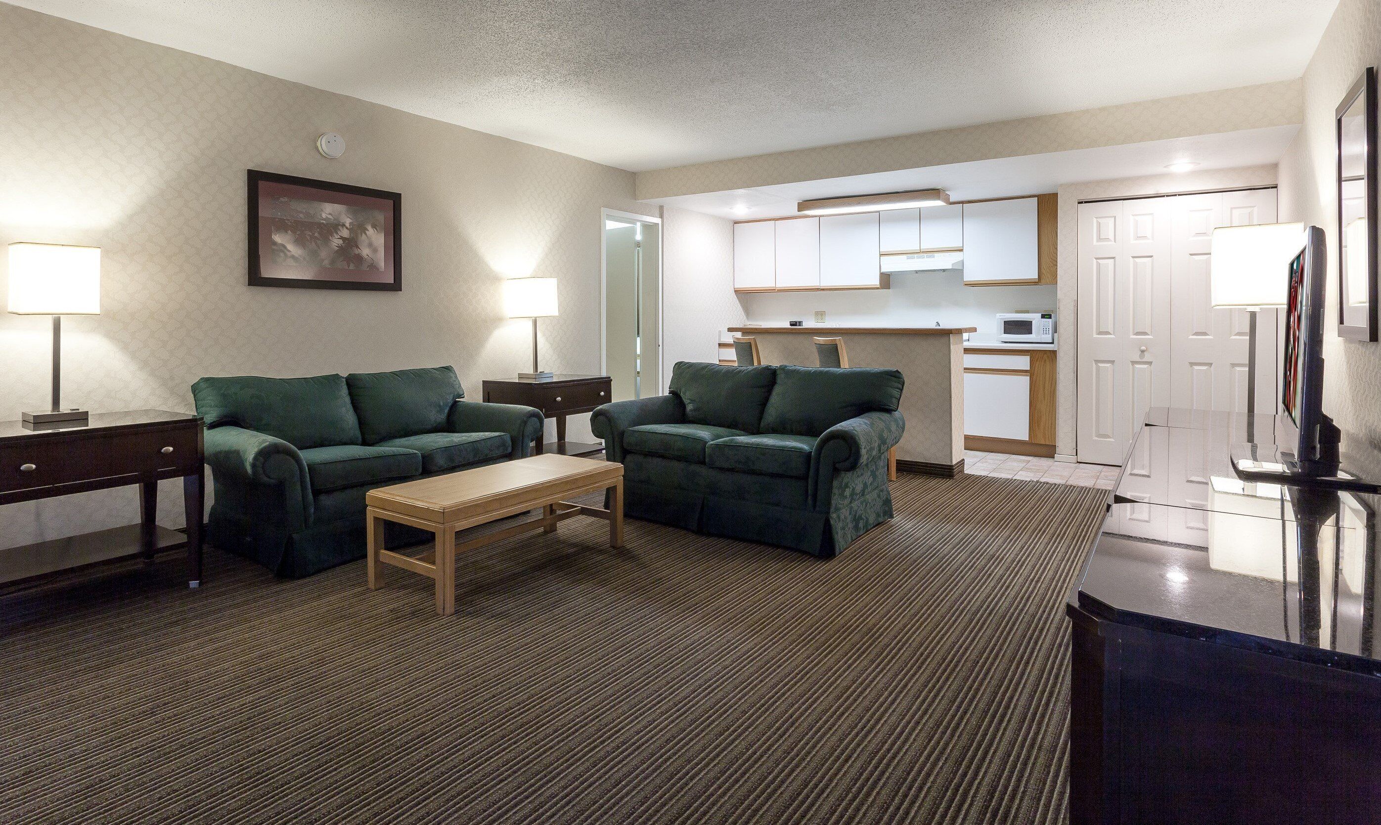 A living room with two green sofas, a wooden coffee table, and a TV on a stand.