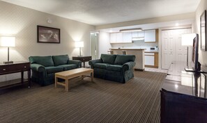 A living room with two green sofas, a wooden coffee table, and a TV on a stand.