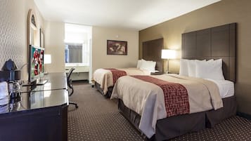 Een hotelkamer met twee bedden, een bureau met een computer, een televisie en een raam.