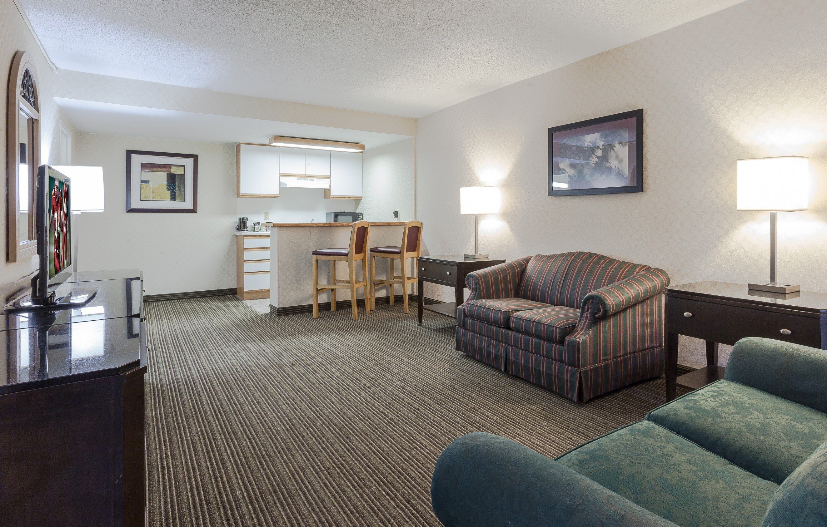 A hotel room with a kitchenette, a sofa, a desk, and a chair.