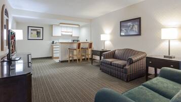 A hotel room with a kitchenette, a sofa, a desk, and a chair.