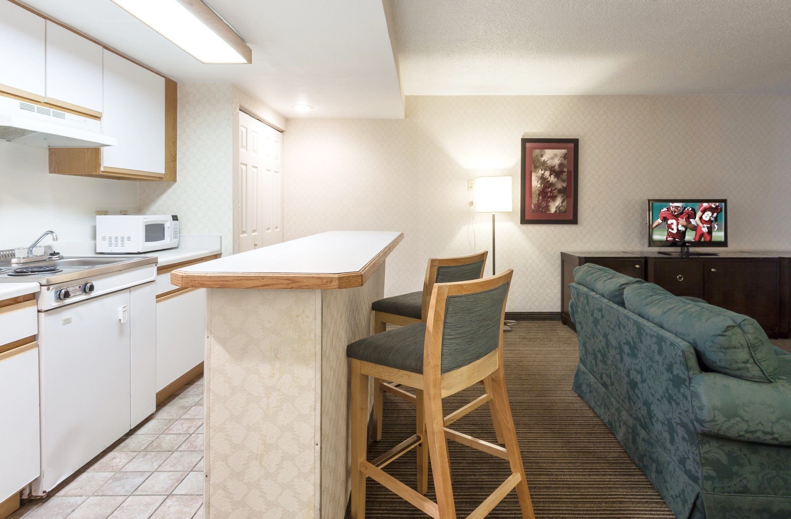A compact hotel room with a kitchenette, a dining area, and a seating area with a sofa and chairs.