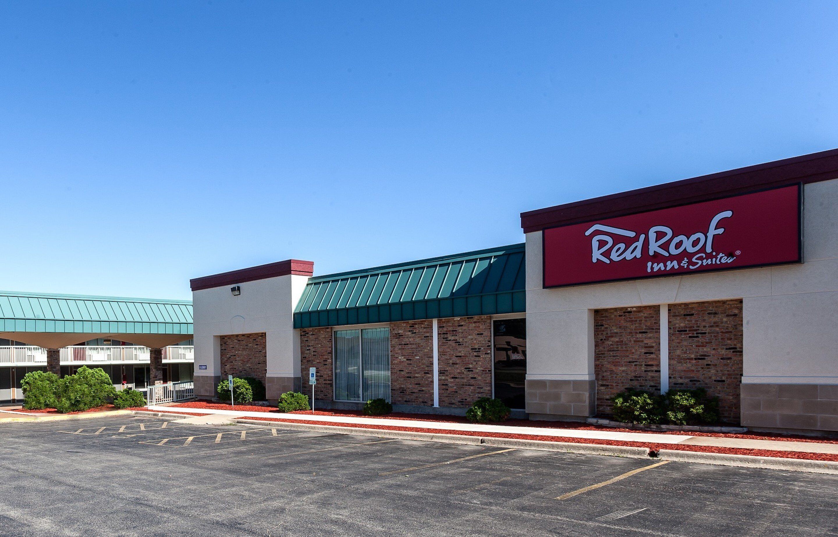 Un bâtiment de la chaîne Red Roof Inn & Suites, doté d’un toit végétalisé, d’une façade en briques et d’un parking situé à l’avant.