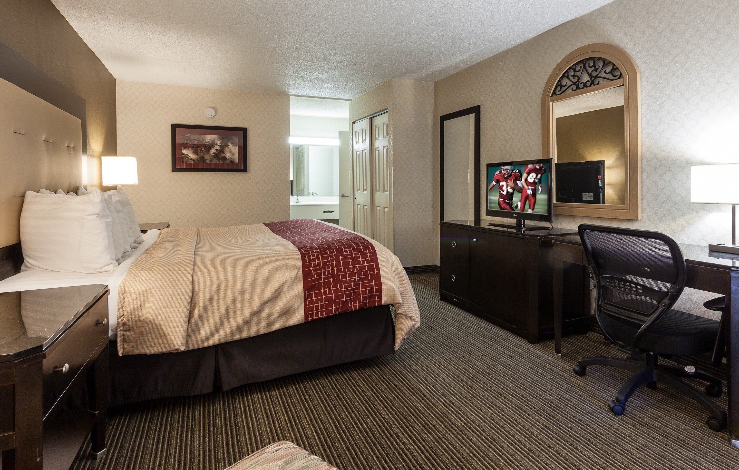 Una habitación de hotel con una cama, un escritorio con computadora, televisión y espejo.