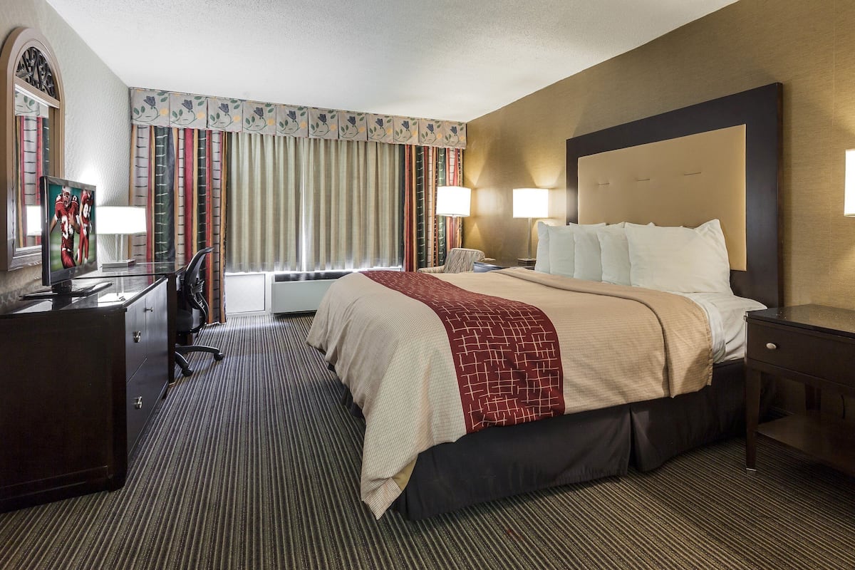 A hotel room with a large bed, two bedside lamps, a desk with a television, and a window with curtains.