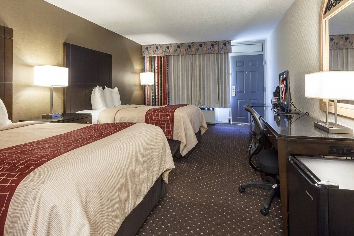 A hotel room with two beds, a desk, a chair, and a television.