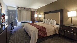 A hotel room with a large bed, bedside lamps, a desk with a flat-screen TV, and a window with curtains.