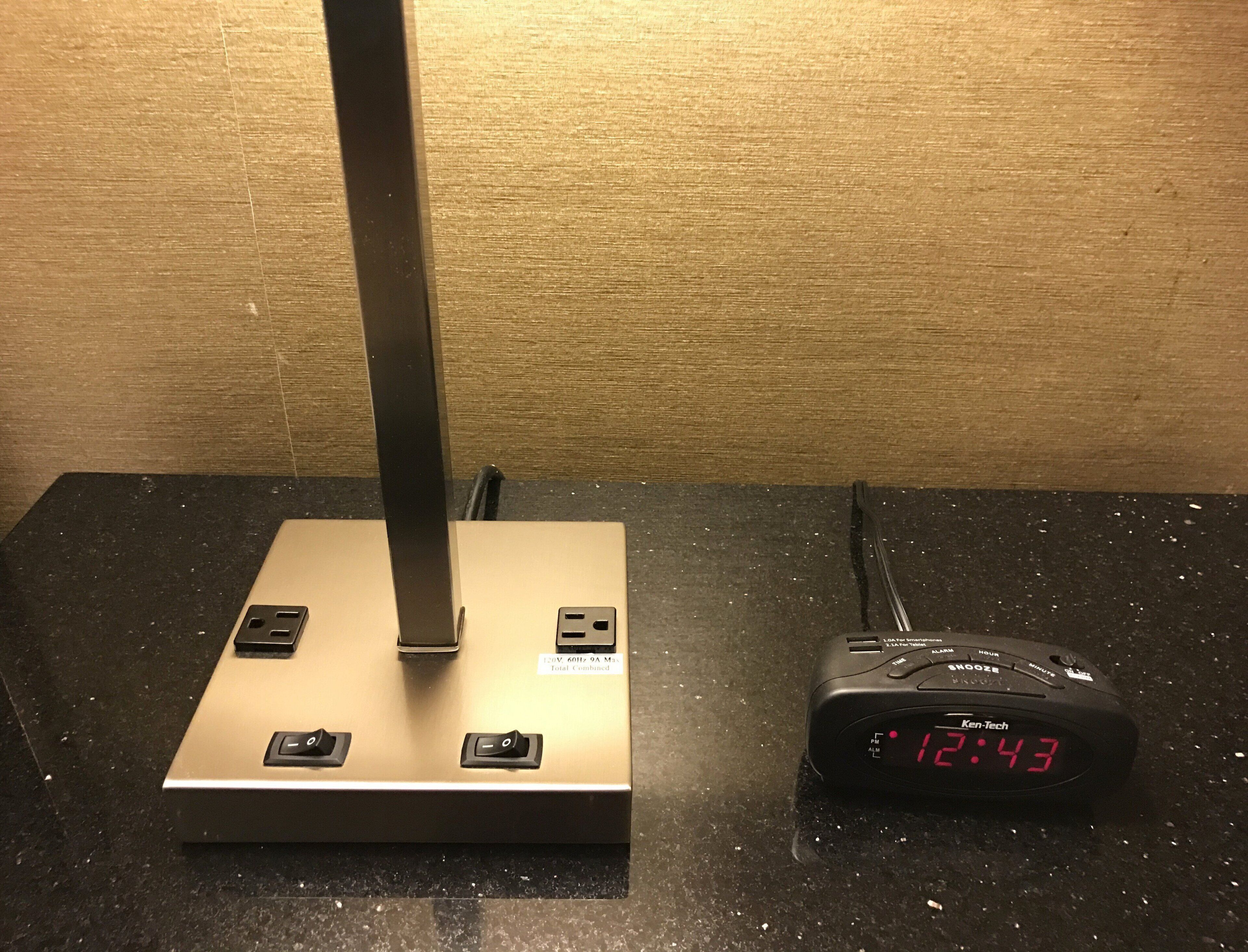 A power strip with a digital clock displaying 12:43, a lamp, and a wall socket.