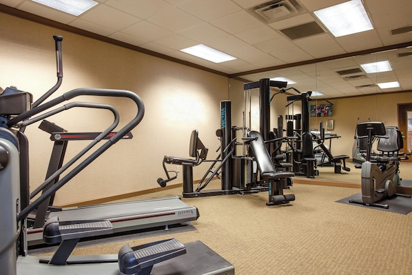 Un gimnasio con equipo de cardio, máquinas de pesas y un espejo grande.