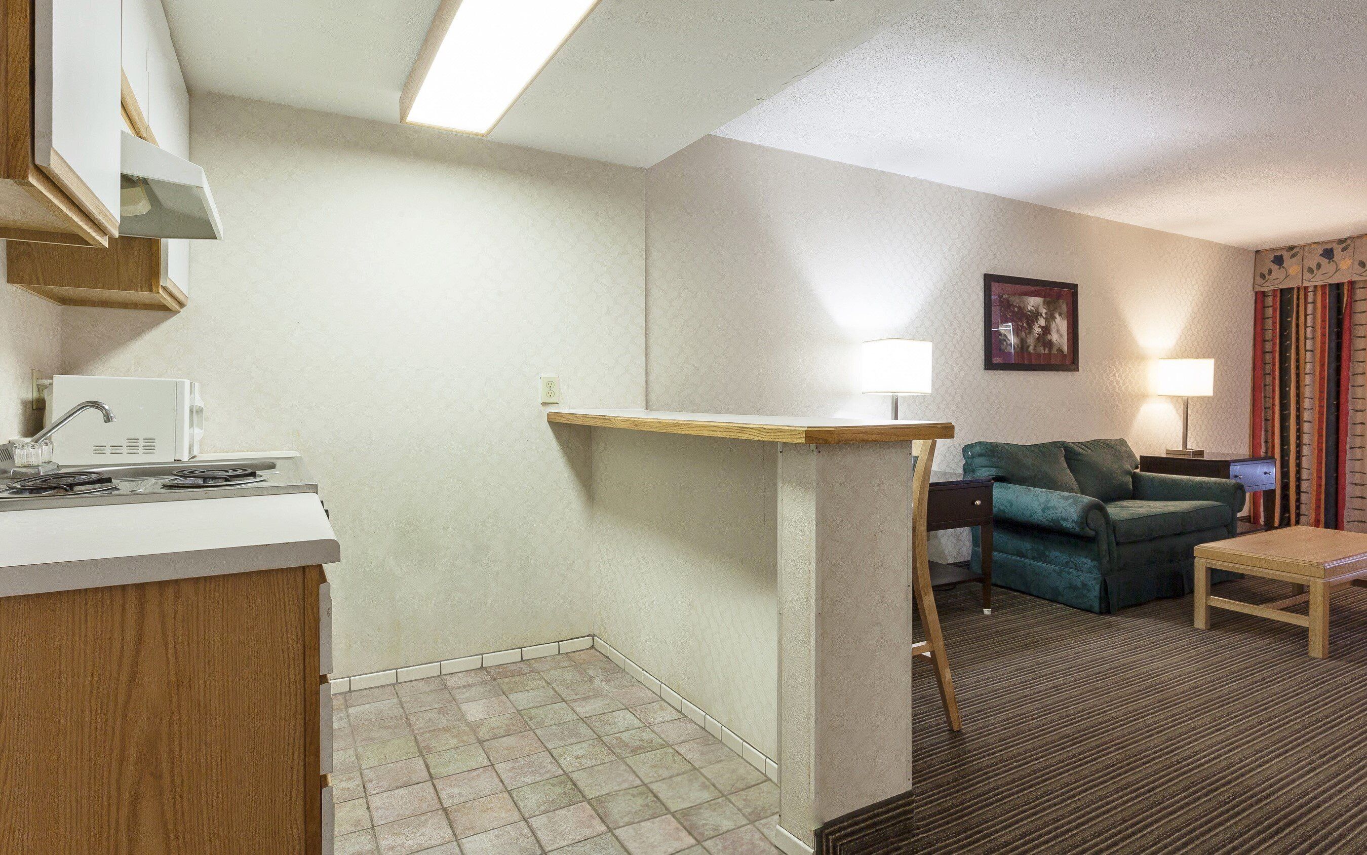 Une chambre d’hôtel équipée d’une kitchenette, d’un canapé, d’une petite table et d’une lampe.