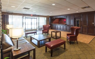 Un vestíbulo de hotel con sillones de cuero, una mesa de centro de madera, un banco y una lámpara.