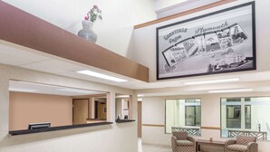 A reception area with a reception desk, two patterned armchairs, a large framed welcome sign, and a vase with flowers on the wall. - Super 8 by Wyndham Plymouth (Plymouth)