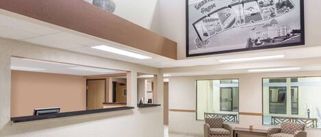 Ein Empfangsbereich mit einer Rezeption, zwei gemusterten Sesseln, einem großen Empfangszeichen im Bilderrahmen und einer Vase mit Blumen an der Wand.