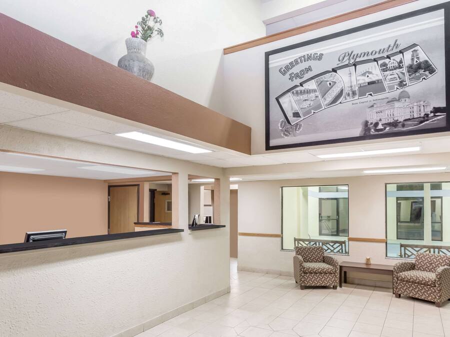 A reception area with a reception desk, two patterned armchairs, a large framed welcome sign, and a vase with flowers on the wall.