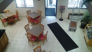 A dining area with multiple wooden tables and red cushioned chairs, a black mat on the floor, and a ladder in the corner. - Super 8 by Wyndham Plymouth (Plymouth)