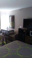 Una habitación de hotel con cama, escritorio, silla, televisión y microondas.