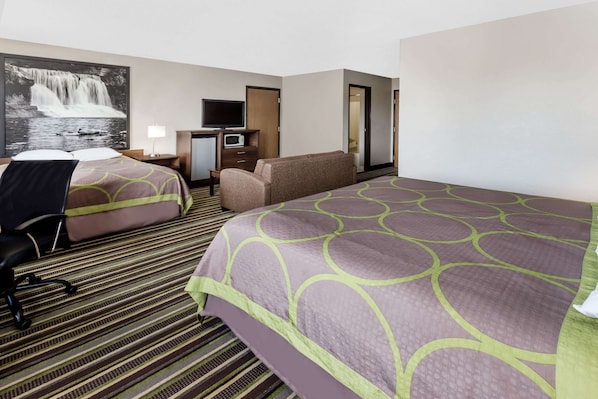 Habitación de hotel con dos camas, un escritorio con computadora, televisor y un cuadro grande de cascada colgado en la pared.