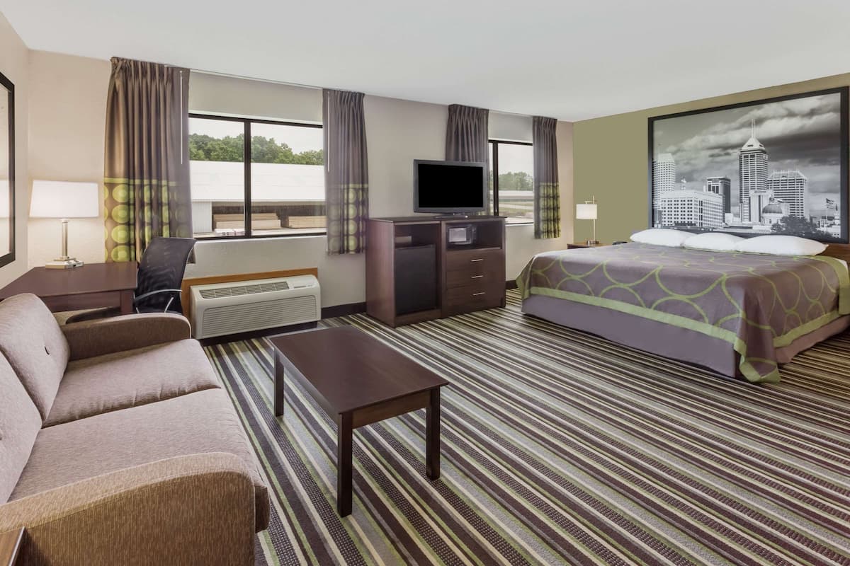 Habitación de hotel con cama, sofá, escritorio, televisor y un amplio ventanal con cortinas.