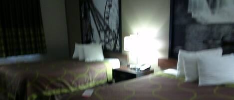 A hotel room with two beds, a nightstand, and a lamp.