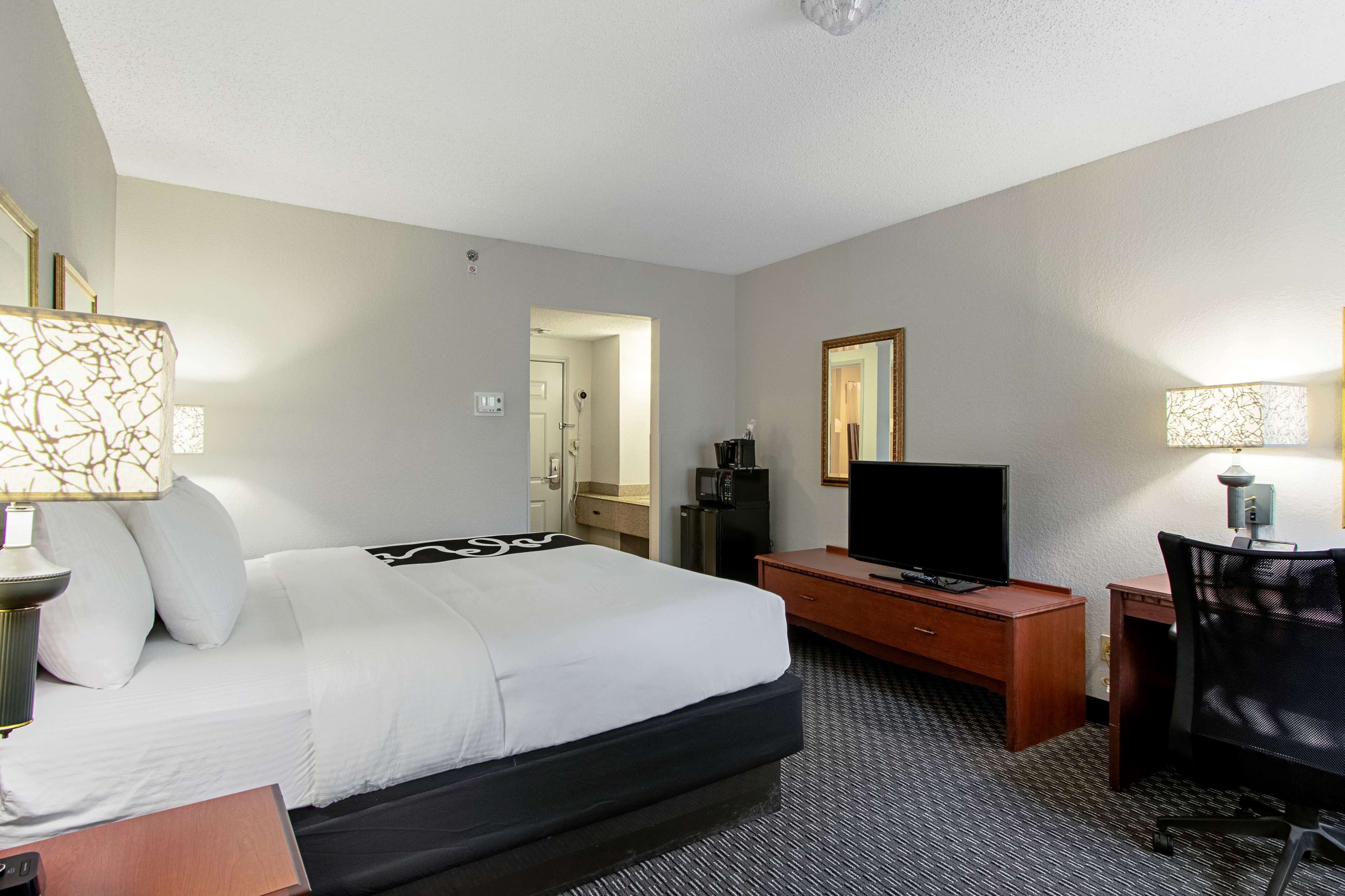 Une chambre d’hôtel avec un lit, un bureau, une télévision et un miroir.