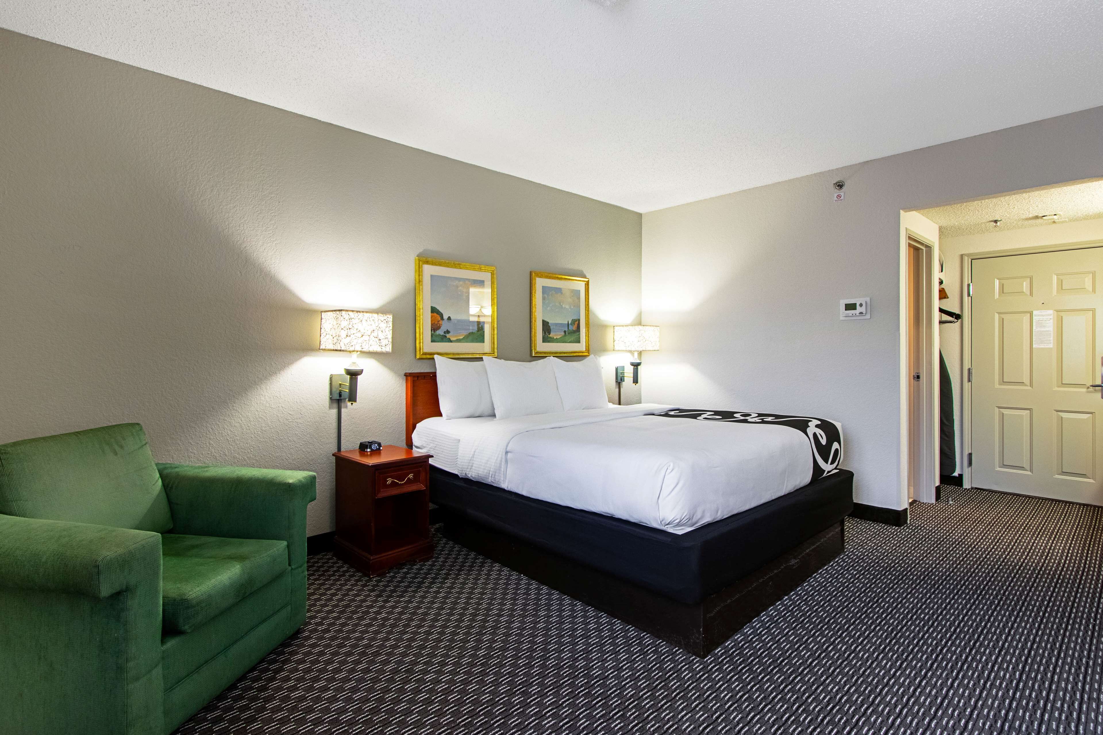 Ein Hotelzimmer mit einem Bett, einem grünen Sessel, zwei Nachttischlampen und zwei gerahmten Bildern an der Wand.