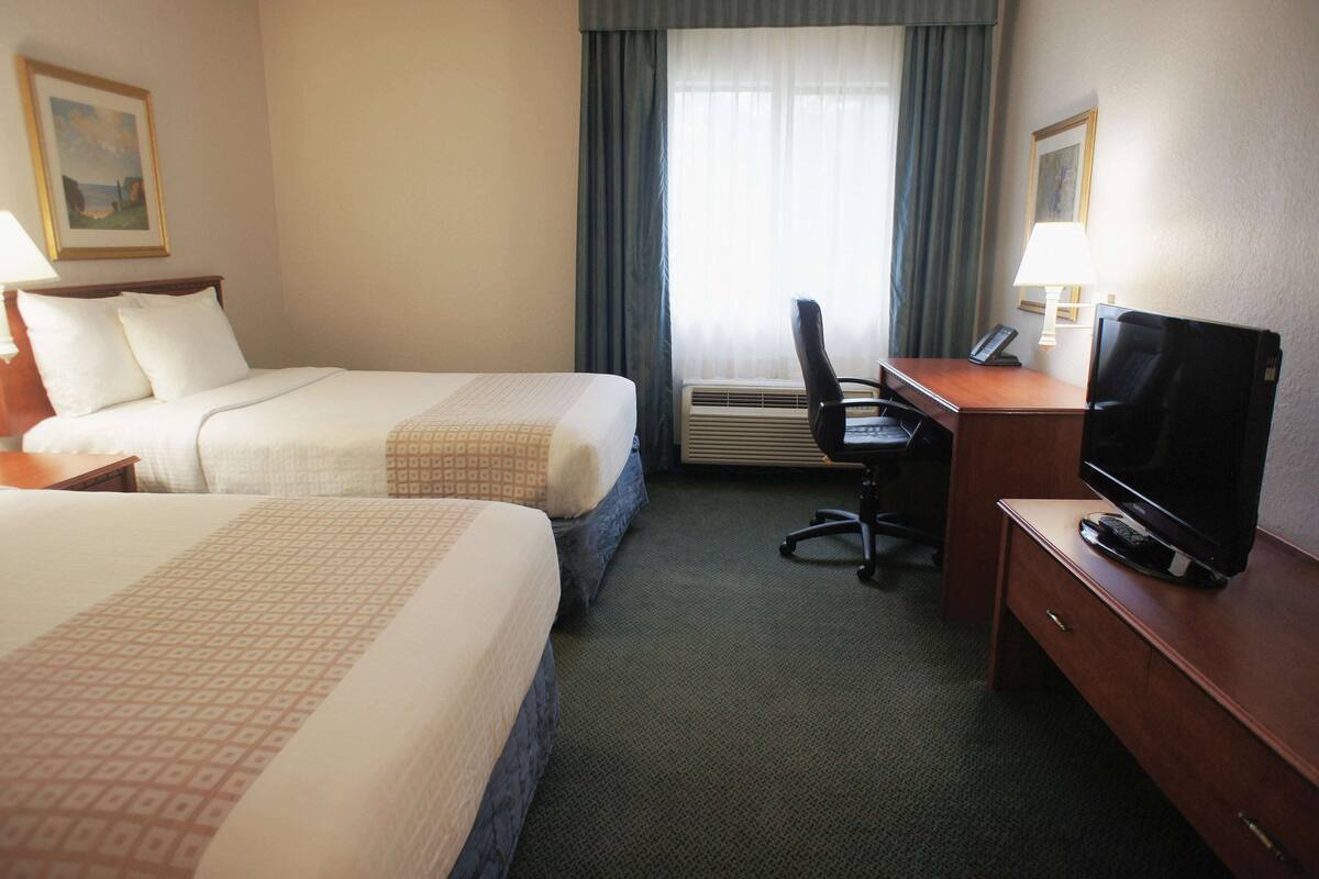 A hotel room with two beds, a desk with a computer, a television, and an air conditioning unit.