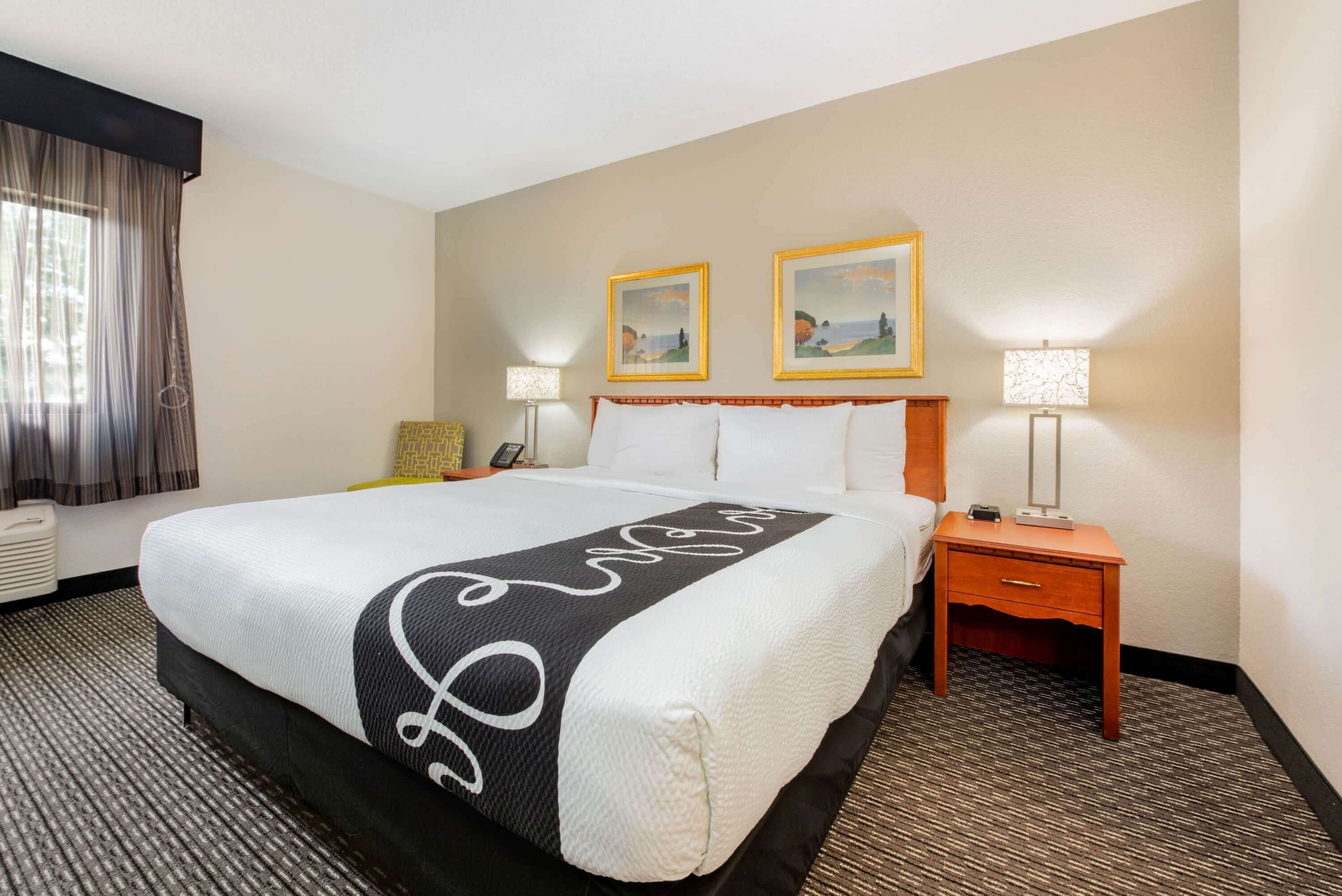 A hotel room with a large bed, two bedside lamps, a nightstand, and two framed pictures on the wall.