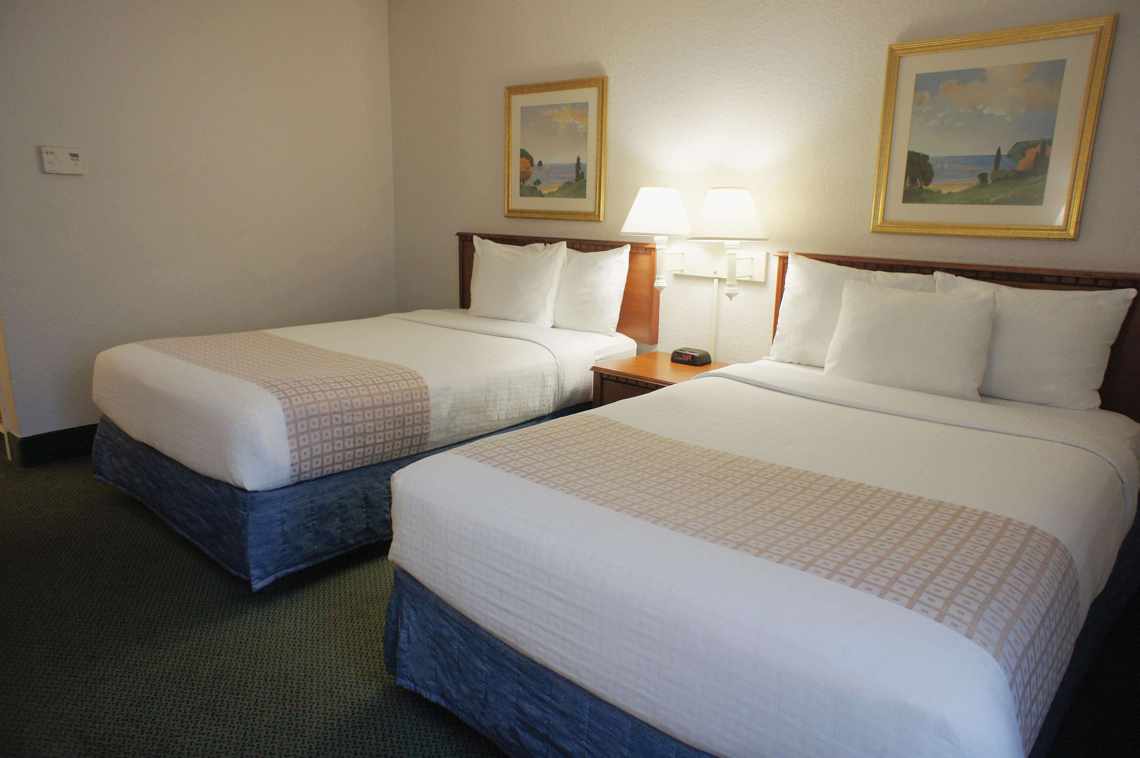 A hotel room with two beds, a nightstand, a lamp, and two framed pictures on the wall.