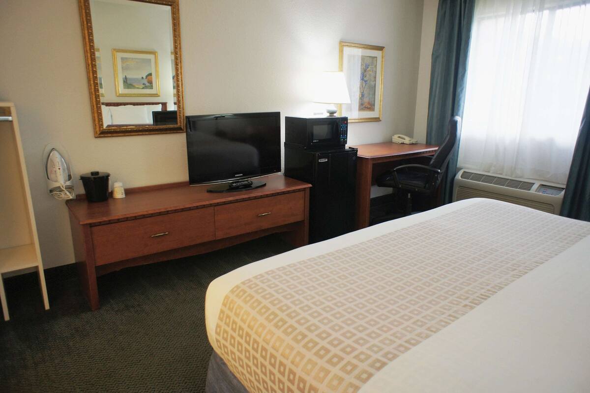 A hotel room with a bed, a desk with a computer and a telephone, a microwave, and a mirror on the wall.