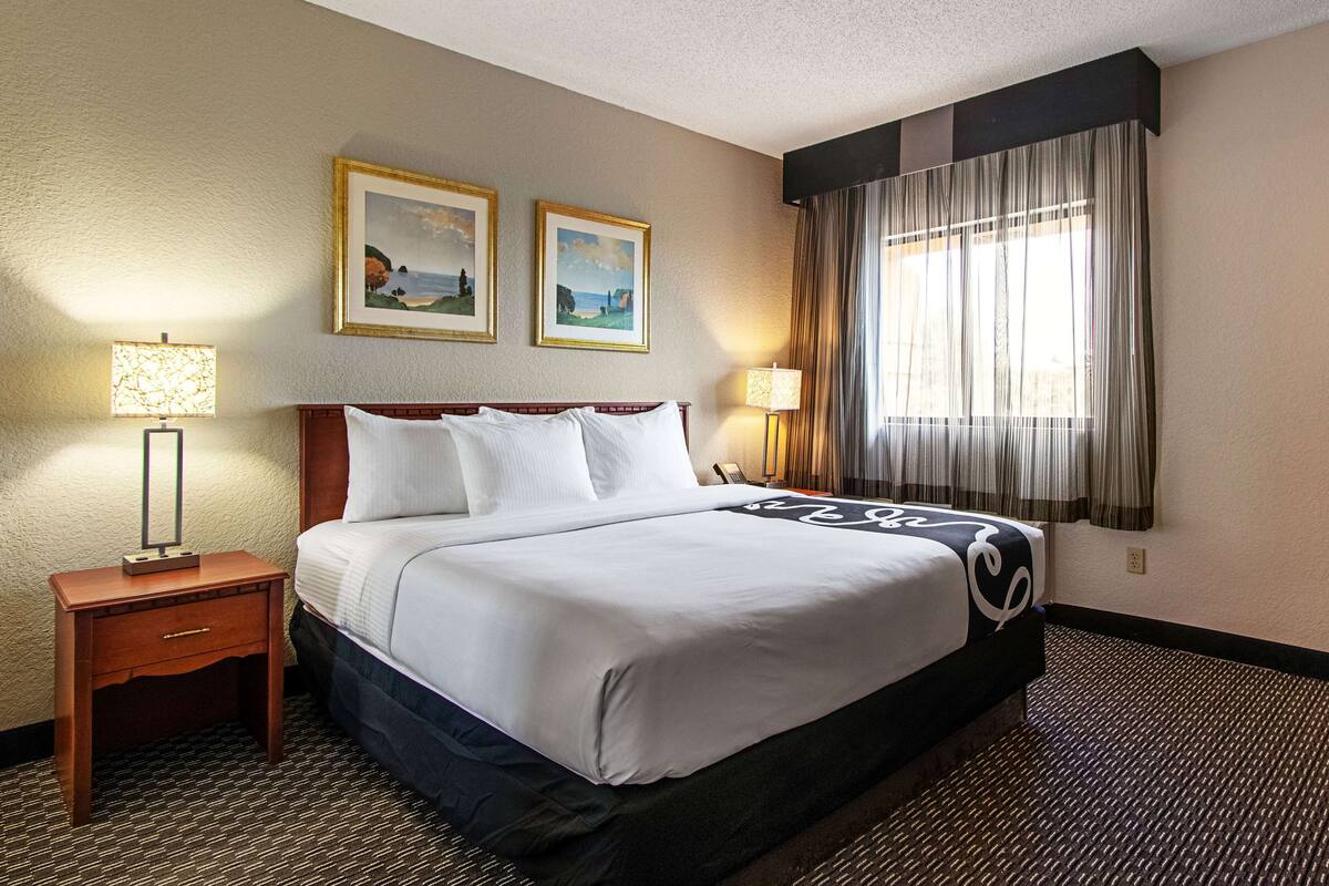 A hotel room with a large bed, two bedside lamps, a nightstand, and two framed pictures on the wall.