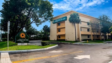 A hotel named LaQuinta Inn with a sign, a parking lot, and a building with multiple floors.