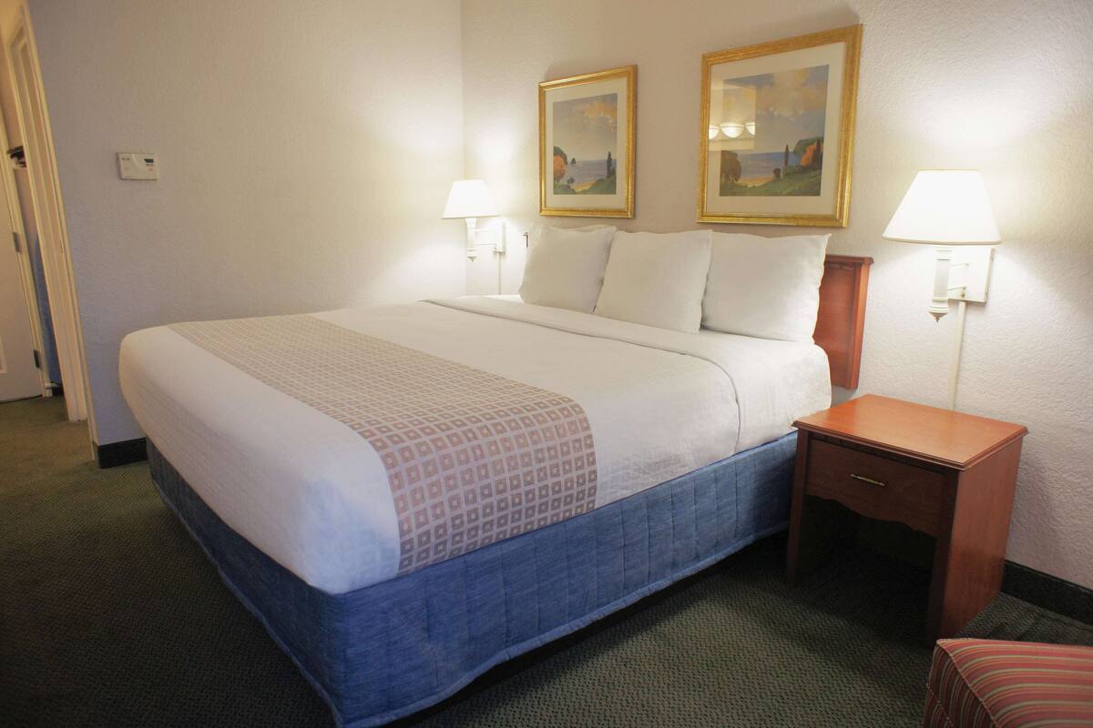 A hotel room with a bed, a nightstand, two wall-mounted lamps, and two framed pictures on the wall.